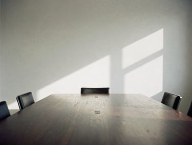An empty, quiet boardroom flooded with soft side-light, a single dark oak table reflecting the light, architectural shadows, 35mm film.