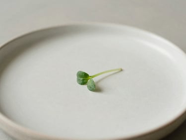 Close-up of a minimalist ceramic plate with a single micro-green garnish, soft natural side lighting, shallow depth of field, warm gray background