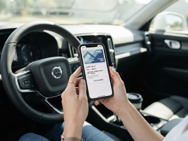 Eye-level medium shot of hands holding a smartphone showing a digital insurance card inside a clean modern vehicle, bright daylight, 35mm lens