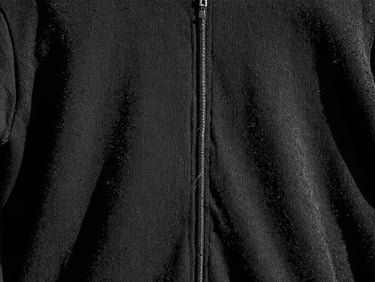 Dettaglio macro di una cucitura rinforzata su un capo di abbigliamento nero, con fili spessi e un leggero effetto distressed, luce dura e ombre nette.