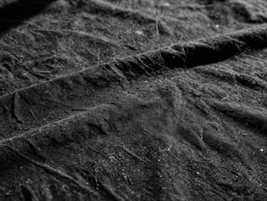 Primo piano macro di un tessuto di cotone nero pesante, con una trama visibile e leggermente rovinata, sotto luce dura e ombre profonde.