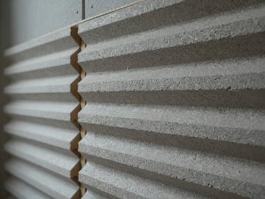 Close-up architectural detail of a residential acoustic wall system showing layered gypsum board and resilient channel assembly, cool studio light, construction detail visible, no people