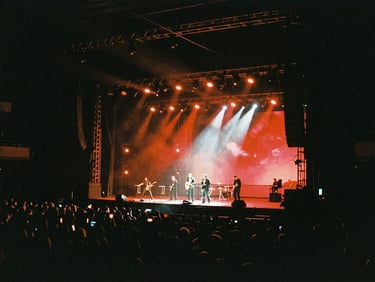 Cinematic film photography, dramatic high-contrast chiaroscuro lighting on a massive live event stage set, deep shadows with rich neon-red accents, anamorphic lens, 35mm