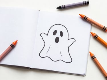 Top-down flat-lay of a children's coloring book with a Halloween theme, open to a page with a cute ghost, surrounded by orange and black crayons, bright natural daylight.