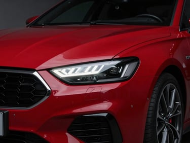 Close-up of a crimson red sports sedan's front grille and headlight, aggressive styling, low-key studio lighting, sharp reflections.
