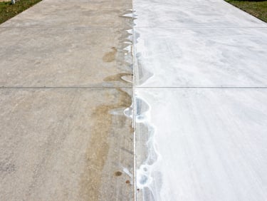 Close-up overhead shot of commercial concrete driveway before-and-after split: left half visibly stained, right half freshly pressure-washed to near-white, bright midday light, no people