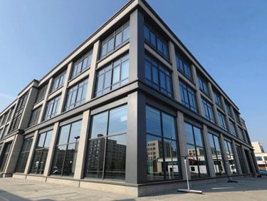 Wide-angle exterior view of a multi-story commercial building with freshly cleaned floor-to-ceiling windows reflecting clear blue sky, professional squeegee equipment visible at lower right, bright daylight
