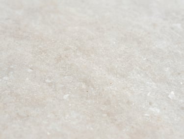 Extreme close-up of an engineered quartz slab surface, uniform warm white with fine aggregate visible, photographed under north-facing daylight showing consistent texture across the frame, no staging