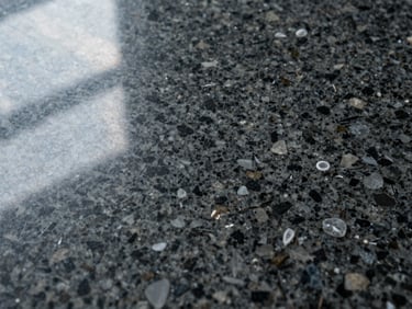 Extreme close-up of a polished granite slab surface, black and grey mineral grain with flecks of quartz catching north-facing window light, no staging, no human presence