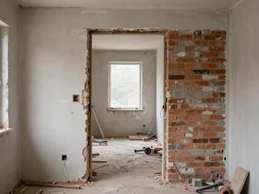 Wide angle of a gutted interior doorway under renovation, fresh plaster on one side, exposed brick on the other, tools on the floor, diffuse daylight from a window at the end of the corridor