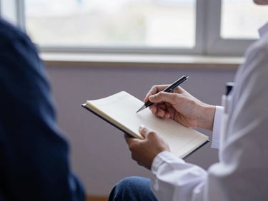 A psychologist's hands gently holding a notebook and pen, suggesting active listening and thoughtful guidance, in a modern, quiet office setting, soft natural window light, muted navy and slate-lilac tones, shallow depth of field, 35mm