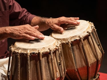 Close-up of a performer's hands on a tabla in active performance, warm golden side-light, dark studio background, the skin of the drum visible in sharp focus, no face shown