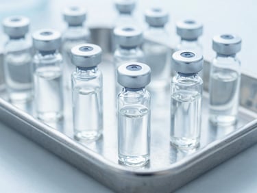 Close-up of sterile glass vials with clear liquid medicine on a stainless steel laboratory tray, cool blue tones, shadowless lighting, 35mm