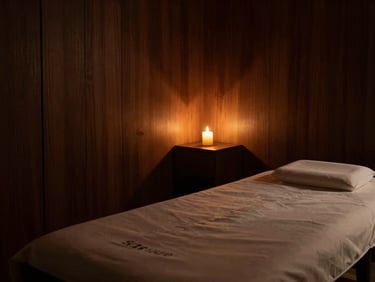 Low-key, moody environmental shot of an empty private treatment room at Spa Star Luxe, warm candlelit glow casting long soft shadows on dark wood walls, minimalist luxury.