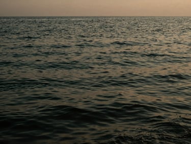 Abstract texture of dark water rippling gently under a low evening sky, deep green and charcoal tones.