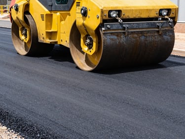 Close-up of a massive yellow road roller compacting fresh textured hot-mix asphalt under bright South African sun