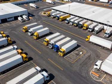 Overhead drone shot of a massive completed commercial logistics parking lot, crisp white and yellow road markings, heavy delivery trucks parked neatly