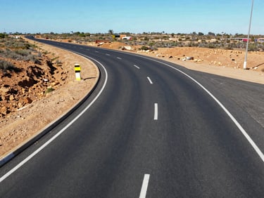 Overhead drone shot of a newly paved asphalt municipal road with crisp white road markings, sweeping curves, clear South African sky