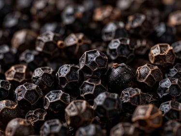 Macro close-up of high-density black pepper corns, showing texture and sheen, dramatic side-lighting, rich deep tones.