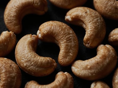 Macro close-up of premium whole cashew nuts, dramatically side-lit, rich deep tones, 35mm, elegant luxury aesthetic, showing smooth surface and crisp edges.