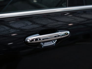 Tight macro shot of a polished chrome door handle of a black executive sedan, reflecting airport terminal lights, low-key lighting.