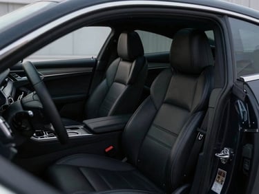 Cinematic interior shot of a pristine black executive sedan cabin, focusing on plush leather seating and subtle ambient light, a briefcase visible on a seat.