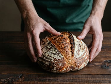 Hands arranging rustic sourdough bread on a dark wooden table, soft natural side-light, moody Scandinavian style, rich tones, 35mm