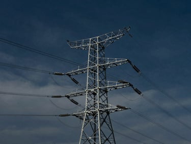 Complex power transmission lines against a dramatic sky, industrial scale, cinematic, premium editorial photography, deep navy and steel tones, architectural framing, 35mm
