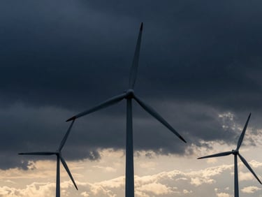 Utility-scale wind turbines at sunset, dramatic sky, low horizon, cinematic, premium editorial photography, deep navy and steel tones, architectural framing, 35mm