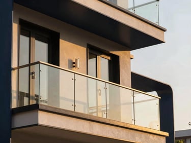 Warm editorial architectural photography of a luxury apartment balcony in Gurugram, golden-hour sunlight streaming through clean glass railings, 35mm lens