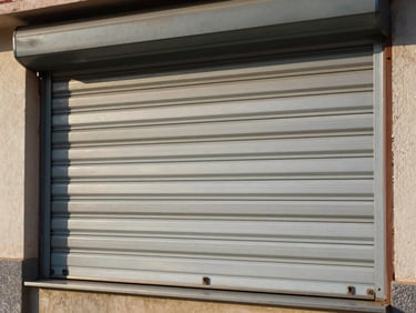 Persiana de seguridad enrollable exterior (roller shutter) descendiendo suavemente sobre ventanal.