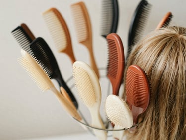Close-up editorial photograph of a neatly arranged collection of various hair combs and a natural-looking wig on a stand, soft natural light.