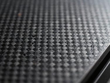 Macro scale photography of a carbon fiber composite layer pattern, showing perfect alignment and zero void spaces under precise industrial lighting.