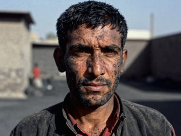 A close-up portrait of a Hazara coal miner in Quetta, coal dust on face, intense eye contact, dramatic high-contrast side lighting, 35mm documentary photography.
