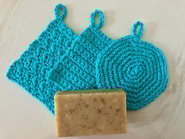 3 crocheted aqua face scrubbies with a bar of soap on top of them