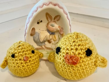2 yellow crocheted chicks with a ceramic Easter egg behind them.