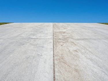 High-contrast before-and-after split of a concrete driveway, clean section vs. dirty section, bright Florida Florida sunlight, vivid blue sky, crisp commercial outdoor photography, sharp focus, high-contrast, 35mm