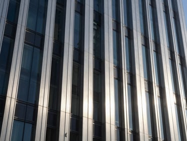 Crisp daylight architectural detail of a modern financial district skyscraper, brushed steel and glass facade, deep shadows, cool silver tones.