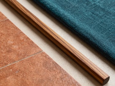 Close-up of tactile interior design materials, including warm terracotta tiles, polished local teak wood, and deep teal handwoven textiles arranged elegantly on a soft ivory surface.