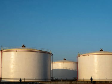 A large oil storage terminal with massive tanks under a clear blue sky, clean geometric lines.