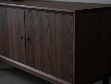 Extreme close-up of a dark fumed oak credenza showing bespoke joinery, dramatic low-key lighting, raw textured wood grain.