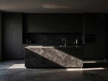 Straight-on view of a monolithic dark stone kitchen island under a single shaft of natural light, deep shadows, minimalist design.