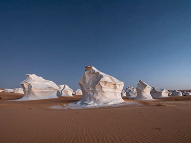Wide environmental shot of surreal white chalk rock formations rising from the desert floor at twilight, starry night sky beginning to appear, deep blue and cool white tones.