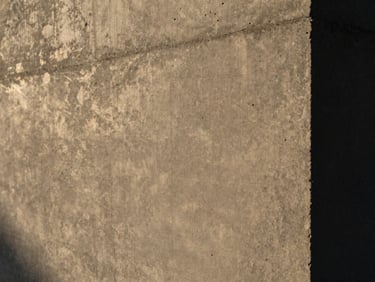 Extreme close-up of raw, textured board-formed concrete with subtle imperfections, warm morning light, low contrast.
