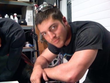 A young don abenante wearing safety goggles on his head in a garage workshop with tools.