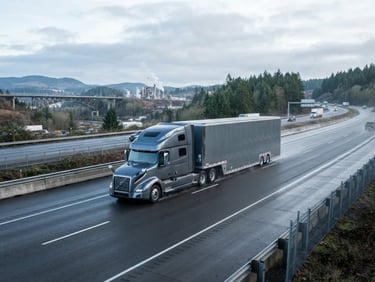 Wide environmental shot of a clean enclosed vehicle transport truck driving down a clear highway under crisp morning overcast daylight, cool metallic tones, sharp industrial detail