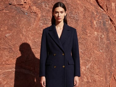 Sharp editorial portrait of a model in a structured navy coat against a harsh Utah red rock cliff, direct midday sunlight, deep shadows, 35mm