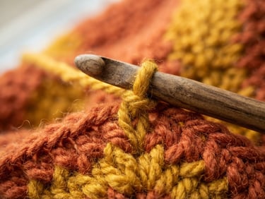 Macro shot of warm terracotta and mustard yellow yarn being crocheted with a wooden needle, soft afternoon sunlight, high texture detail