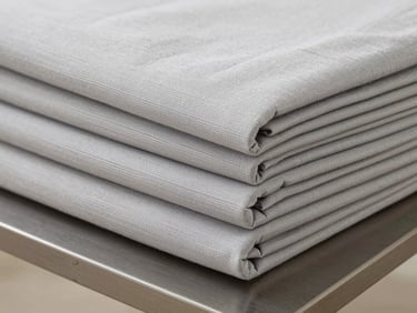 Close-up shot of folded light gray bamboo fiber bedding set, neat stack on a minimalist steel table, soft neutral daylight, detailed textile texture