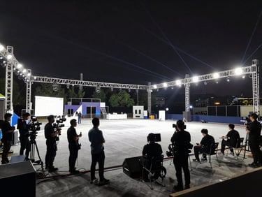 Wide environmental shot of an organized event venue during daytime setup, professional production gear neatly arranged, technicians working under clean stage lights, wide-angle lens.